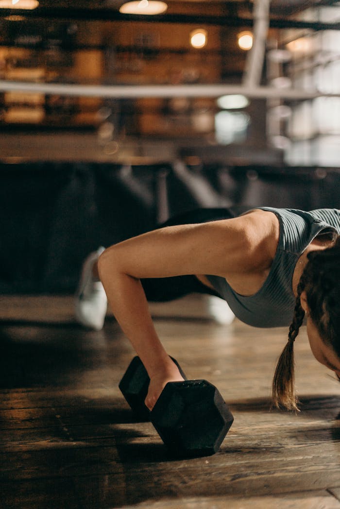 gallery-05 Fit woman doing a dumbbell push-up in a gym, highlighting strength and fitness training.